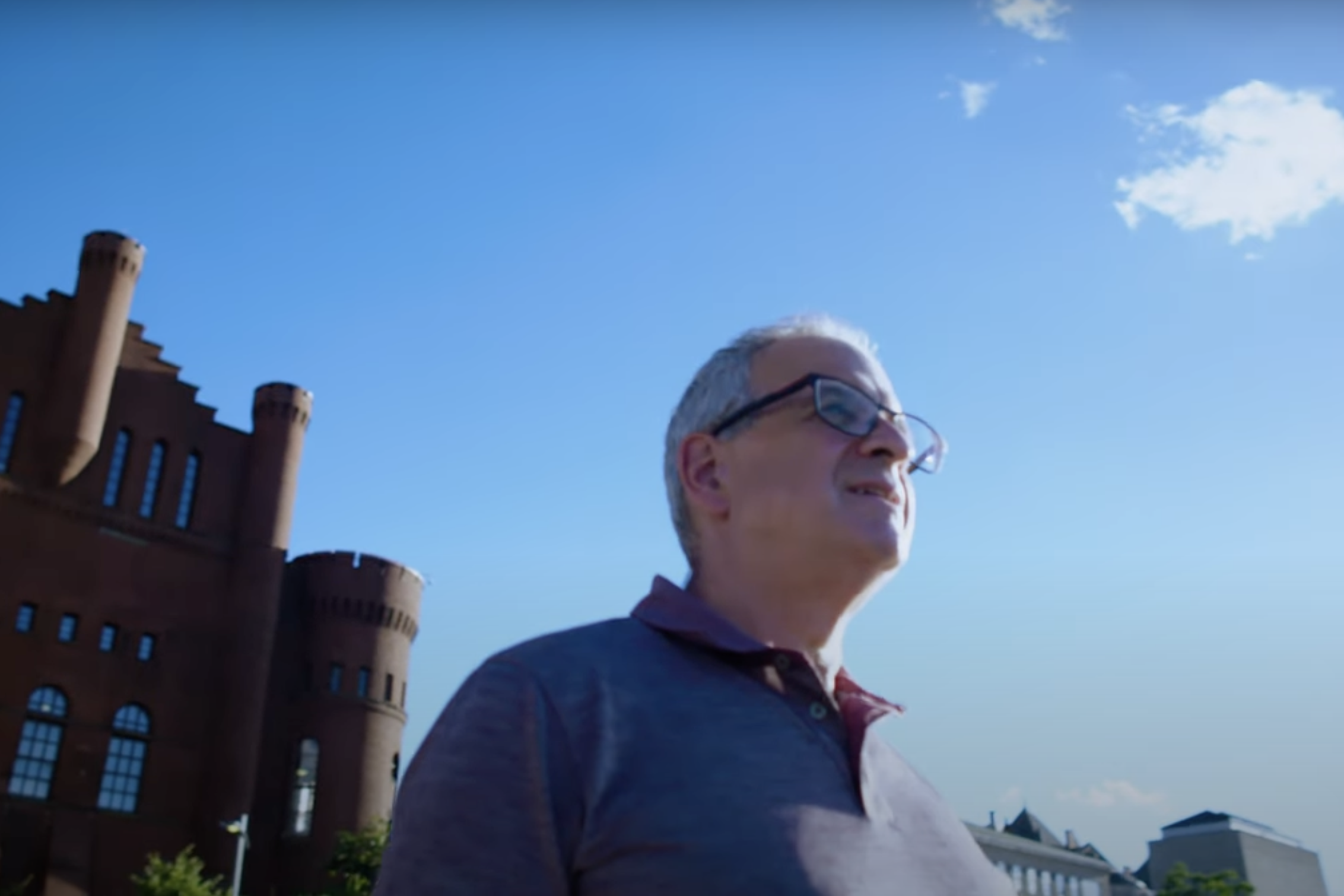 A man stands in front of a blue sky staring out at the distance